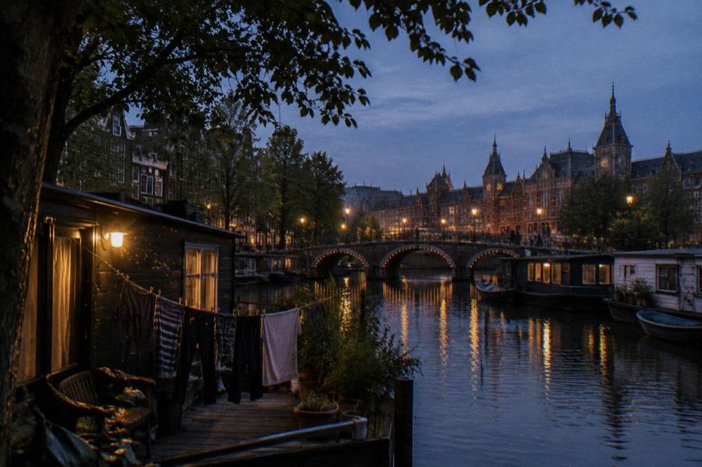 An Amsterdam canal in the evening with arched bridges and lit houseboats