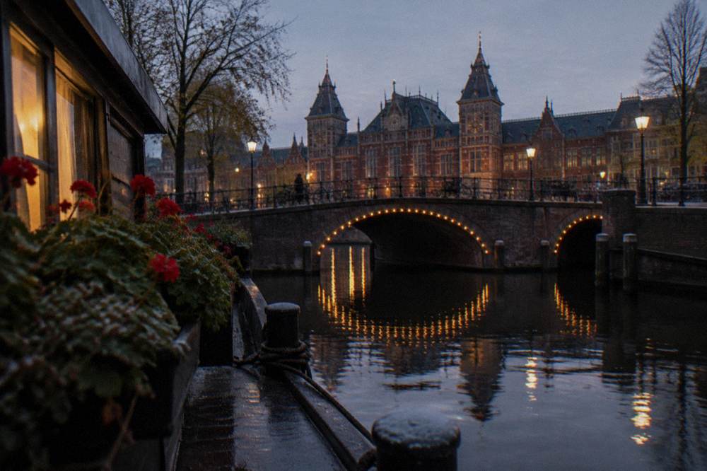 An Amsterdam canal at evening with lit bridges and moored houseboats