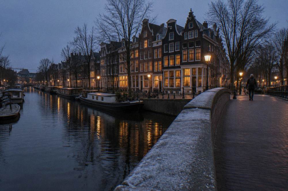 Amsterdam street at dusk with lit windows, a canal bridge and bicycles