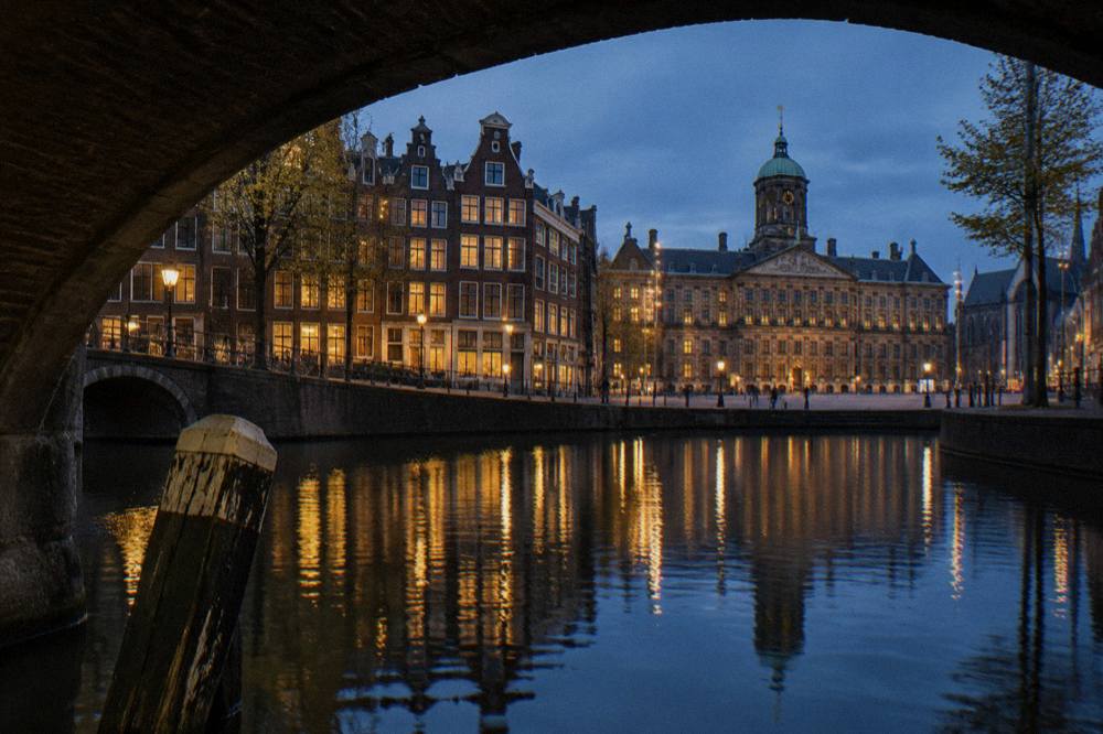 A canal in Amsterdam at dusk with lit bridges and old merchant houses along the water