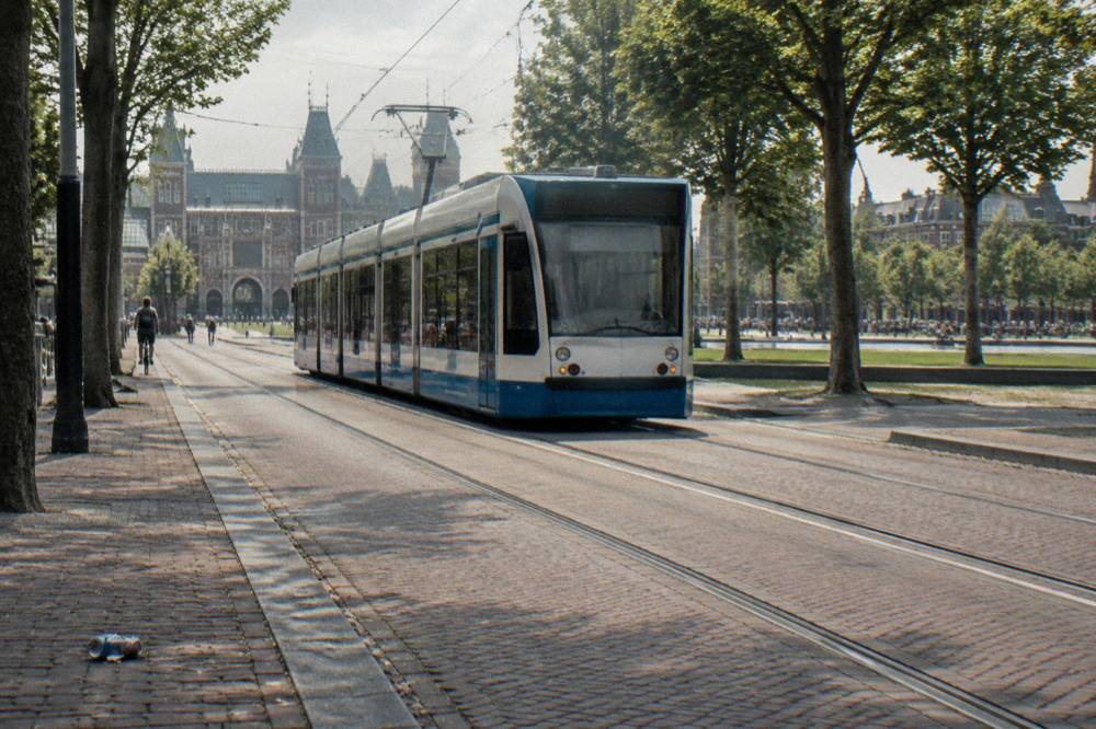 A tram moving along a broad Amsterdam street lined with trees and apartment buildings