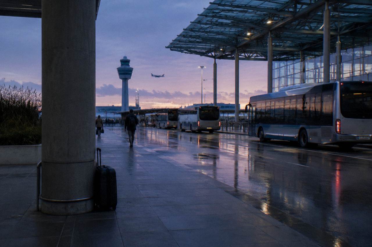 Schiphol airport forecourt at dusk with buses and a station entrance