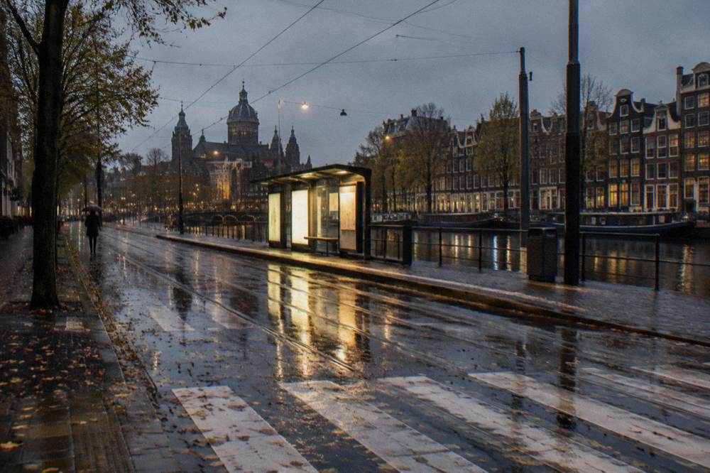 A lit Amsterdam tram stop on an evening street with a bicycle lane