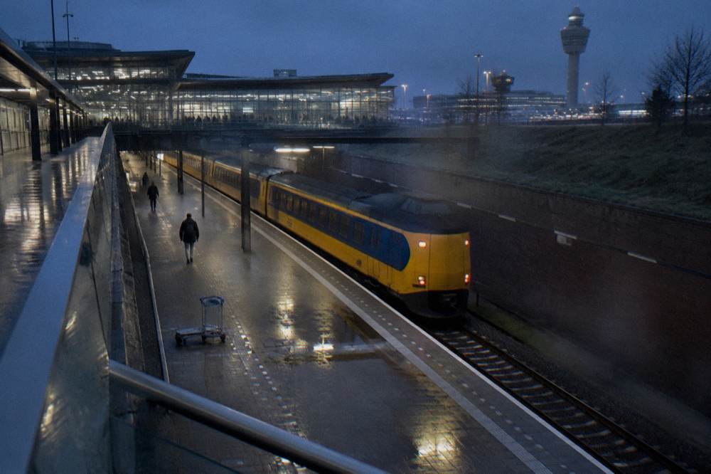 Railway platform at Schiphol Airport station with a train waiting at dusk
