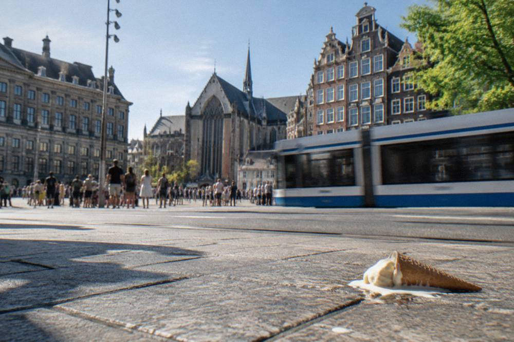 Crowded Amsterdam street corner with trams passing ornate gabled buildings in daytime