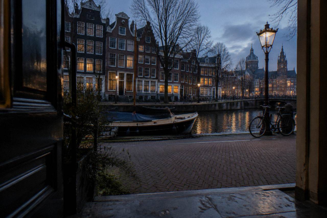 Quiet Amsterdam canal street with narrow brick buildings and bicycles parked along the water at dusk