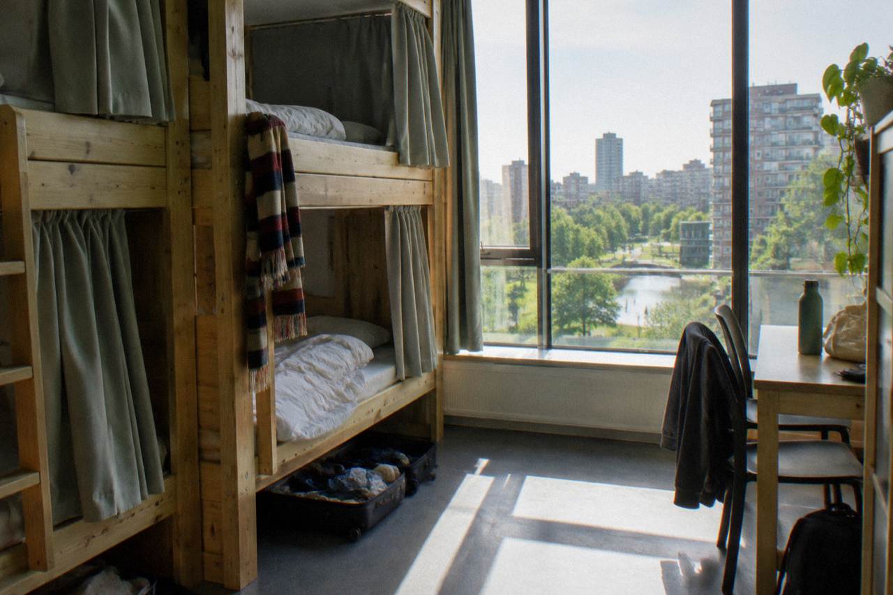 Rows of single beds with privacy curtains in a bright hostel dorm room