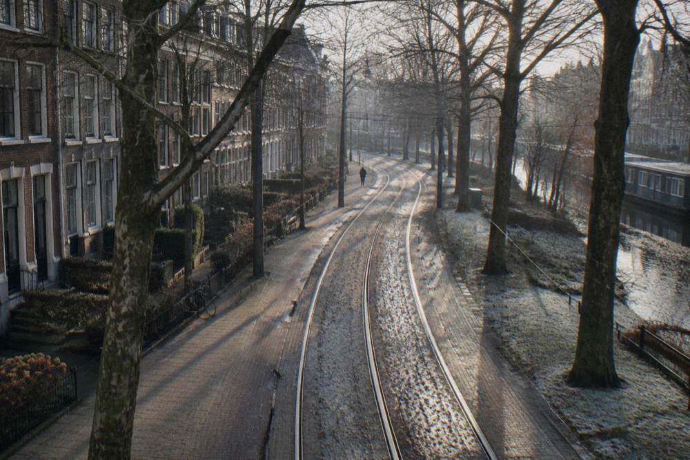 A tram track curving through an Amsterdam East street lined with trees