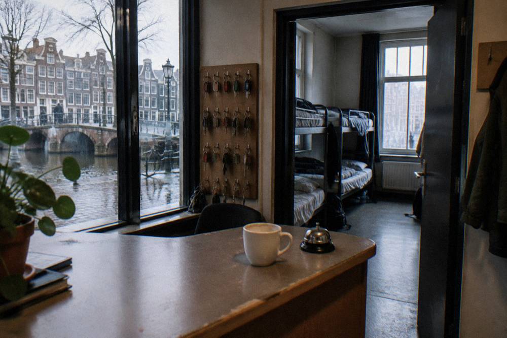 Hostel reception desk with bunk beds visible through an open doorway behind it