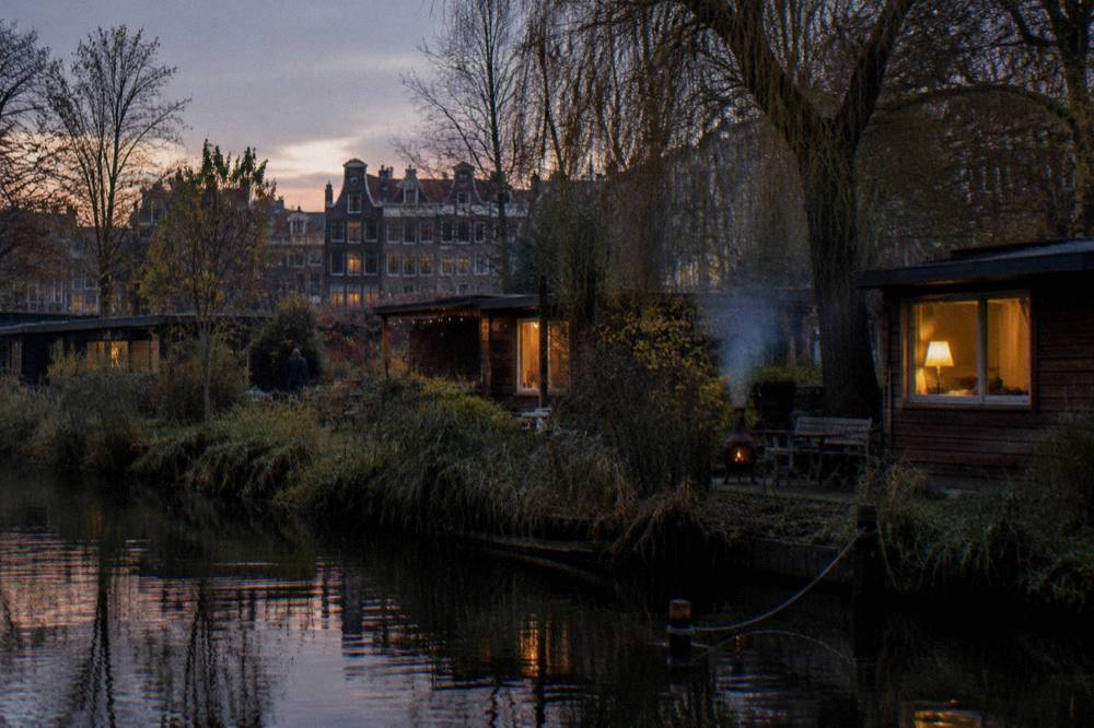 Small wooden cabins beside a canal at a green campsite edge of the city