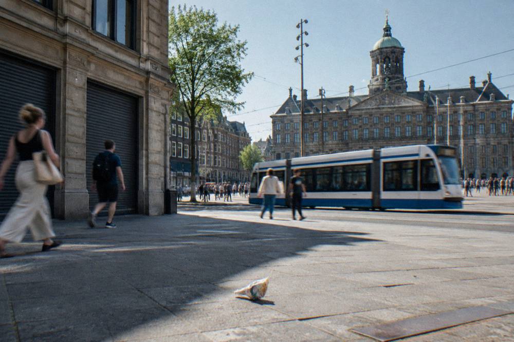A busy central Amsterdam street with trams, cyclists and shopfronts in daylight