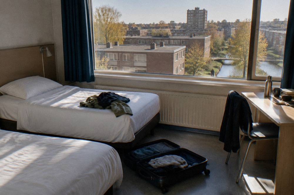 A small tidy hotel room with two single beds and a city window