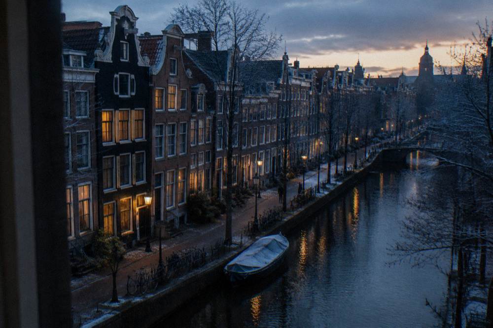 A canal-side street in central Amsterdam with narrow gabled houses at dusk
