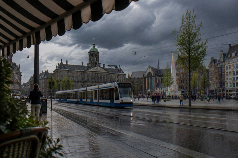 A tram passing narrow shops on a busy Amsterdam street in daylight