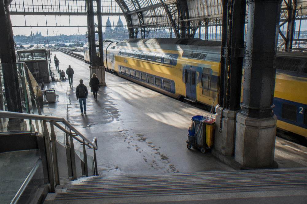 A railway platform with a yellow train waiting beside an airport sign