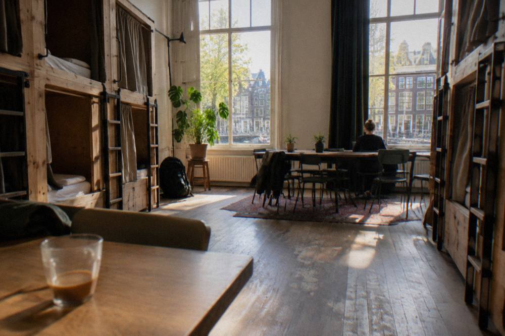 Wooden sleeping pods stacked in two rows inside a bright hostel common space