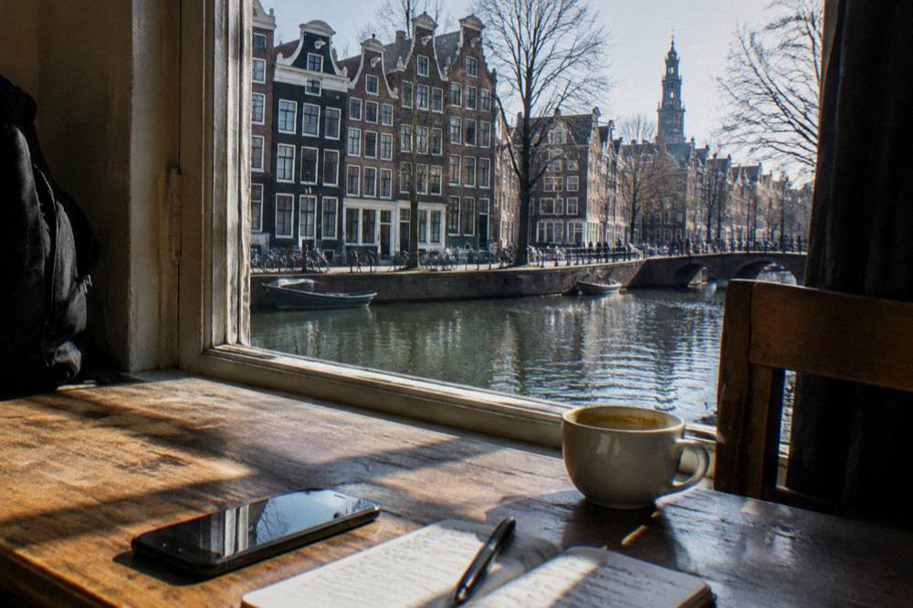 Phone and notebook on a hostel desk beside a window overlooking an Amsterdam canal