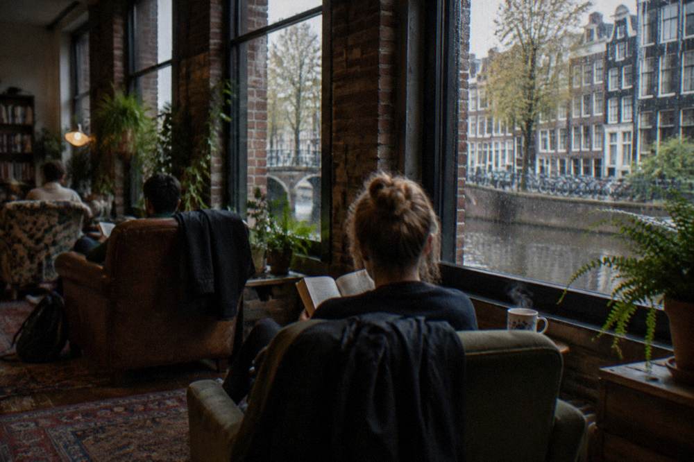 Travellers reading in a hostel lounge with plants and mismatched chairs