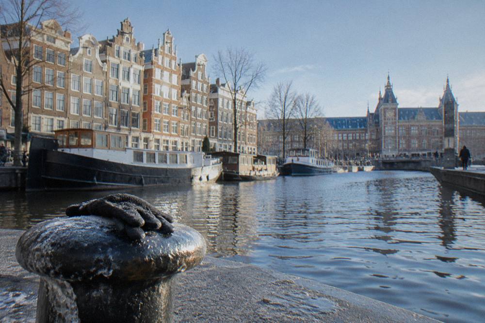 Wide canal street with narrow gabled buildings and bicycles parked along the water a short walk from the station