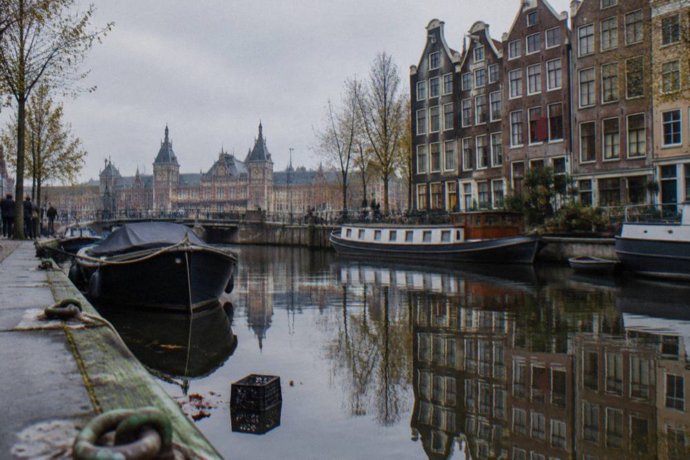 A row of narrow canal houses reflected in still water alongside moored boats