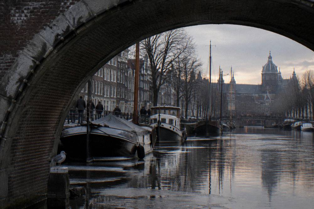 A quiet Amsterdam canal in winter with bare trees and moored boats