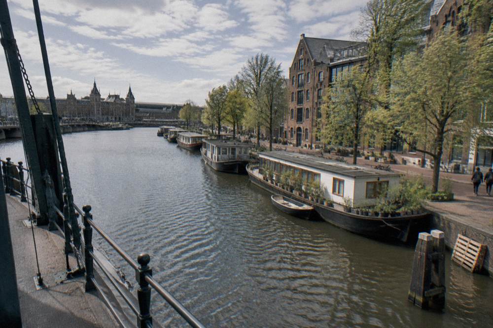 A wide Amsterdam canal junction with houseboats moored along the quay in the eastern islands